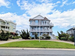 A multi-story residential building with a balcony on the second floor, surrounded by a well-maintained lawn and a clear sky. - 18 South Shore Drive - South Shore Marina (Bethany Beach)