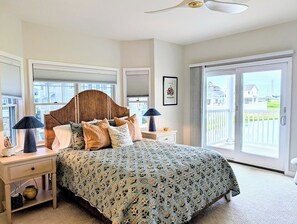 A bedroom with a large bed, a ceiling fan, a nightstand with a lamp, and a view through a sliding glass door. - 18 South Shore Drive - South Shore Marina (Bethany Beach)