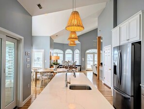 A modern kitchen with a central island, stainless steel appliances, and a dining area with natural light. - 18 South Shore Drive - South Shore Marina (Bethany Beach)