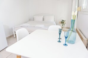 A hotel room with a bed, a white table, and two blue glasses on the table. - Dimitra's cozy studio in old town with backyard! (Agios Pavlos)