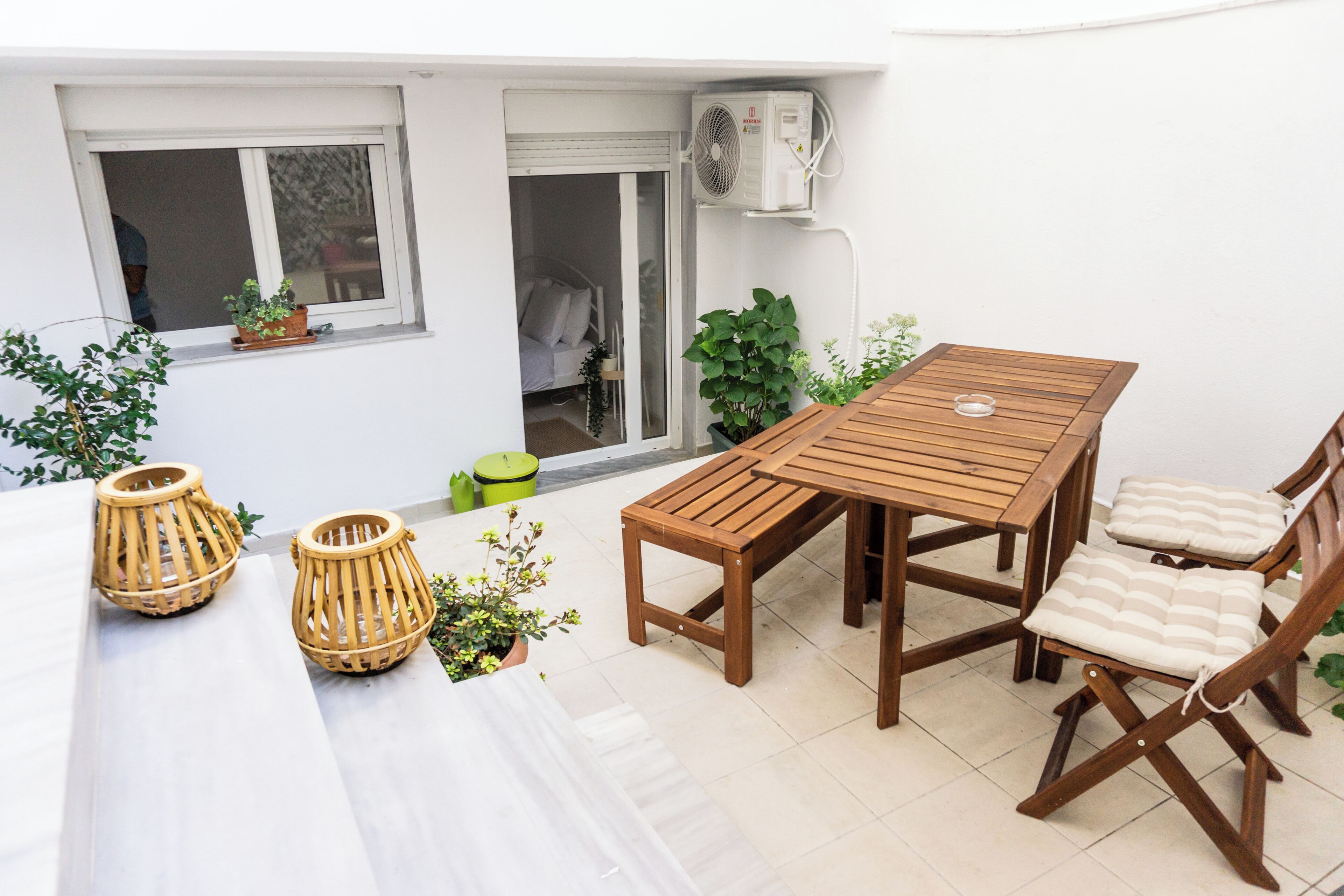 Um pátio com mesa e cadeiras de madeira, rodeado por plantas em vasos.