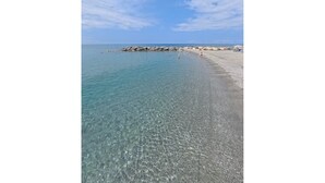 Uma praia com águas claras, um trecho de costa rochosa e algumas pessoas.