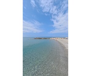 Ein Strand mit klarem Wasser, felsigem Ufer und einigen Personen.