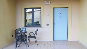 Ein kleiner Sitzbereich im Freien mit Tisch und Stühlen, einer Tür und einem Fenster mit Blick auf ein Gebäude.