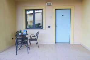 Ein kleiner Sitzbereich im Freien mit Tisch und Stühlen, einer Tür und einem Fenster mit Blick auf ein Gebäude.