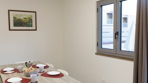 Uma sala de jantar com uma mesa posta para quatro pessoas, um quadro na parede e uma janela com vista para edifícios.