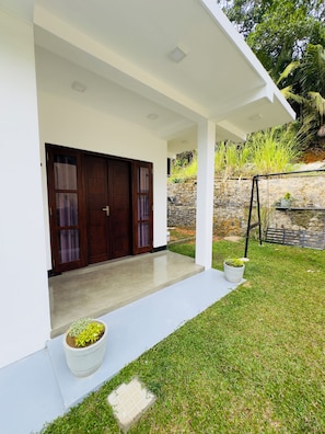Una casa moderna con un porche cubierto, un muro de piedra y un patio con césped.