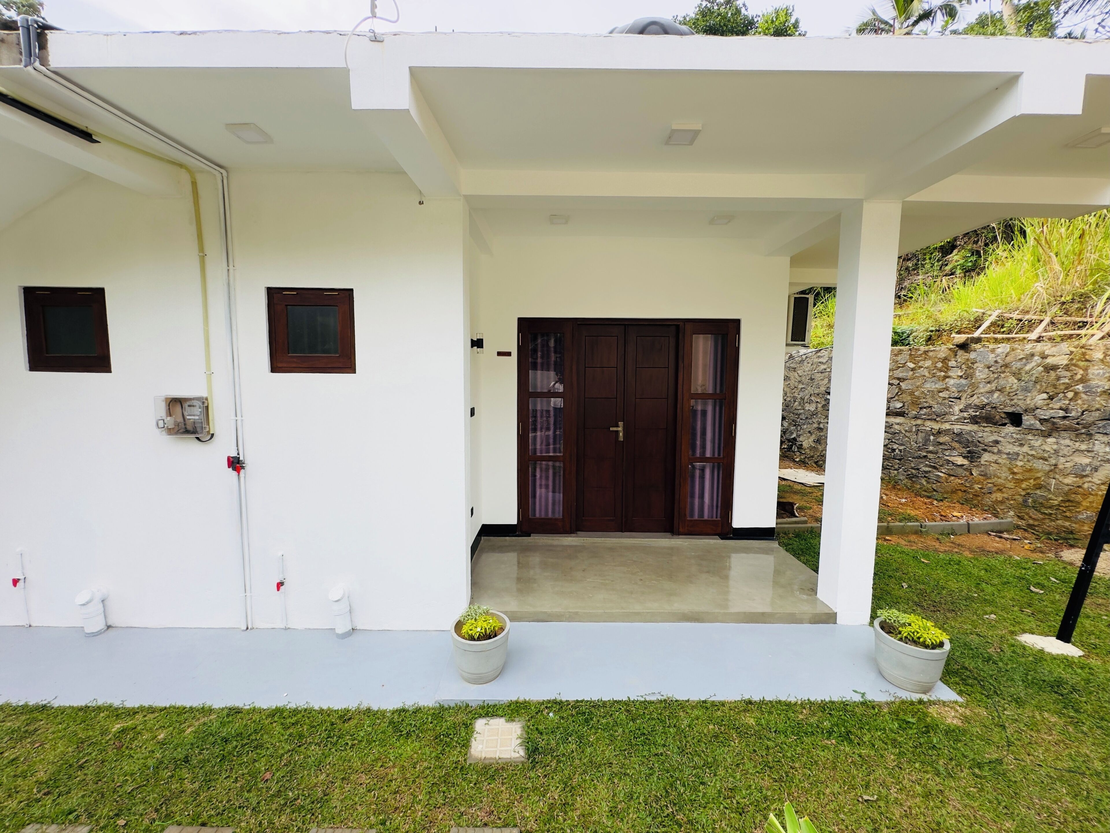 A modern house with a white exterior, a front door with glass panels, and two potted plants on the front porch.