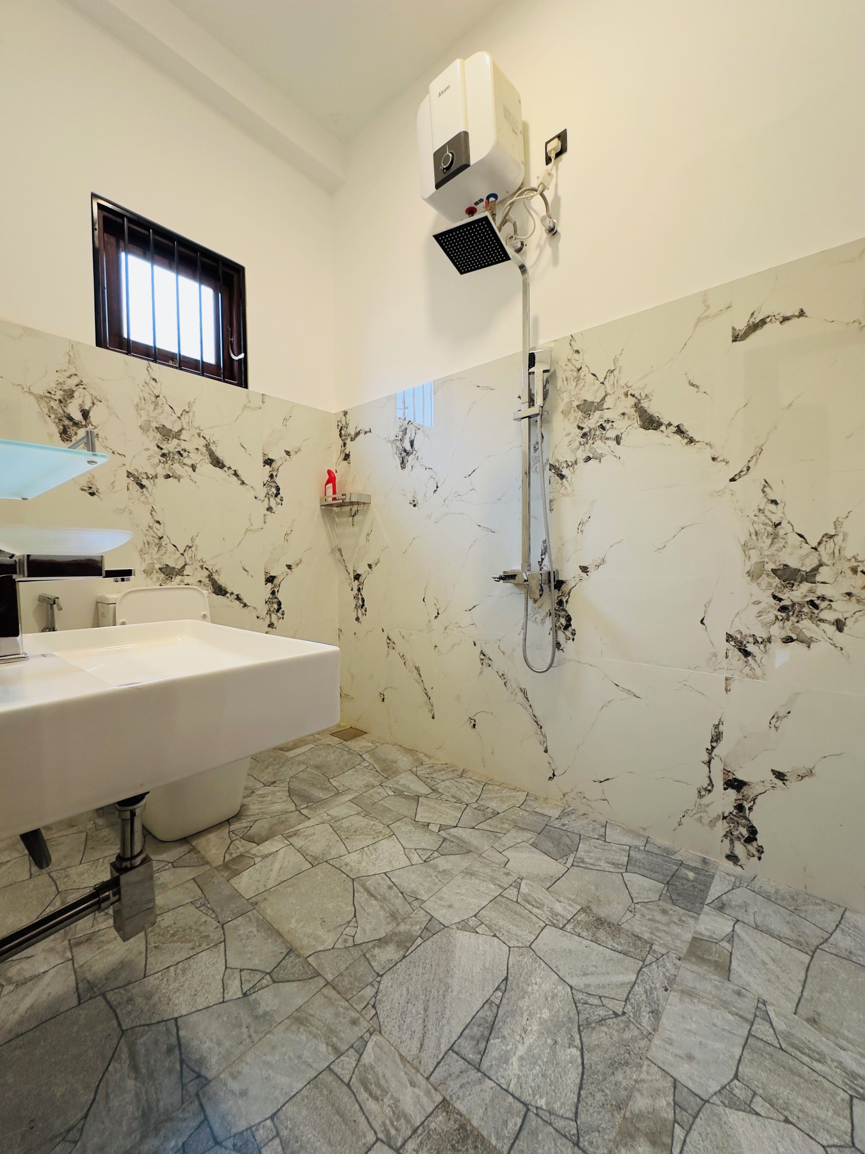 Une salle de bain avec un lavabo blanc, une douchette à main et un climatiseur fixé au mur.