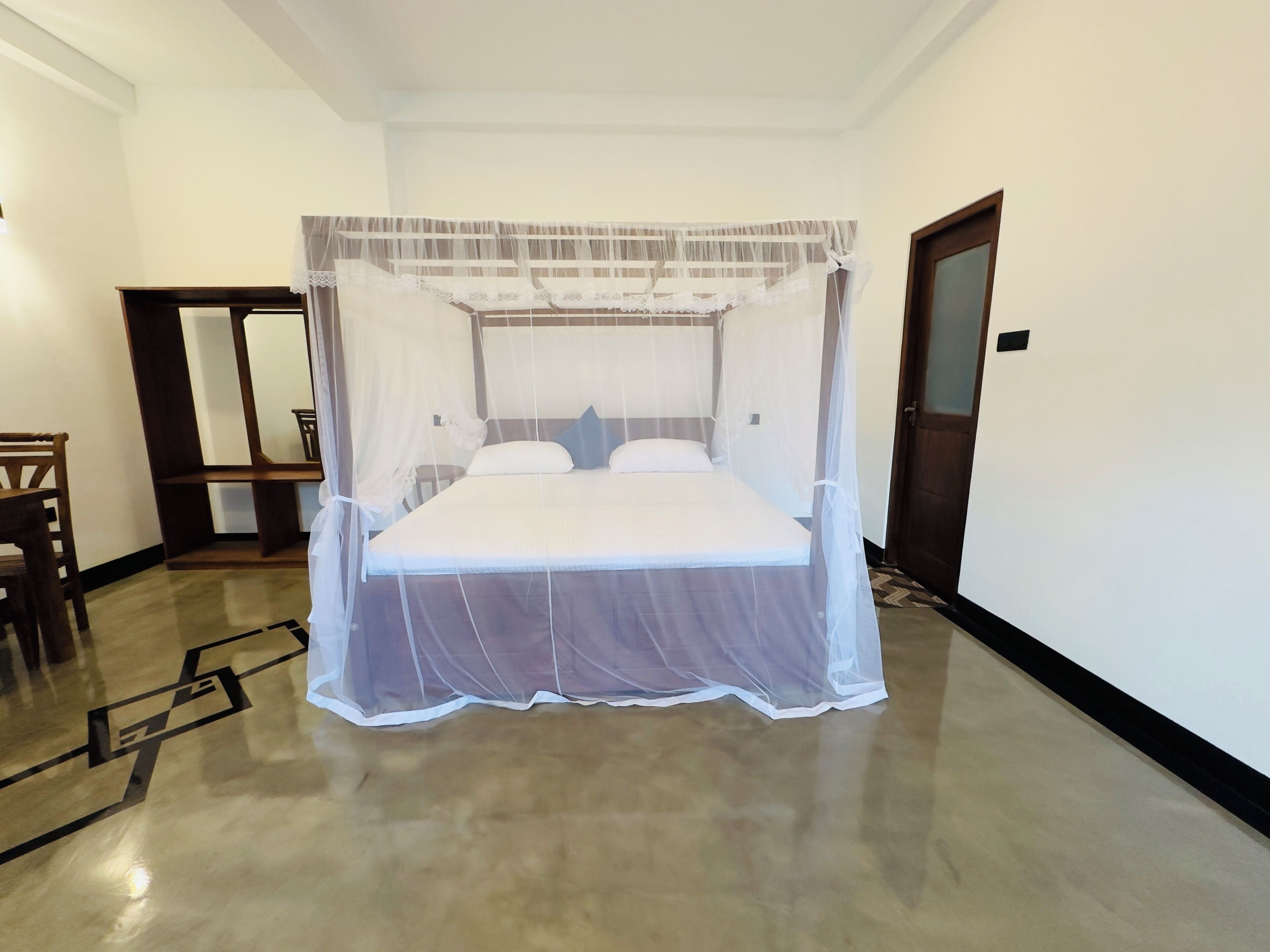 Un dormitorio con una cama bajo un dosel, una silla de madera, un espejo y una puerta.