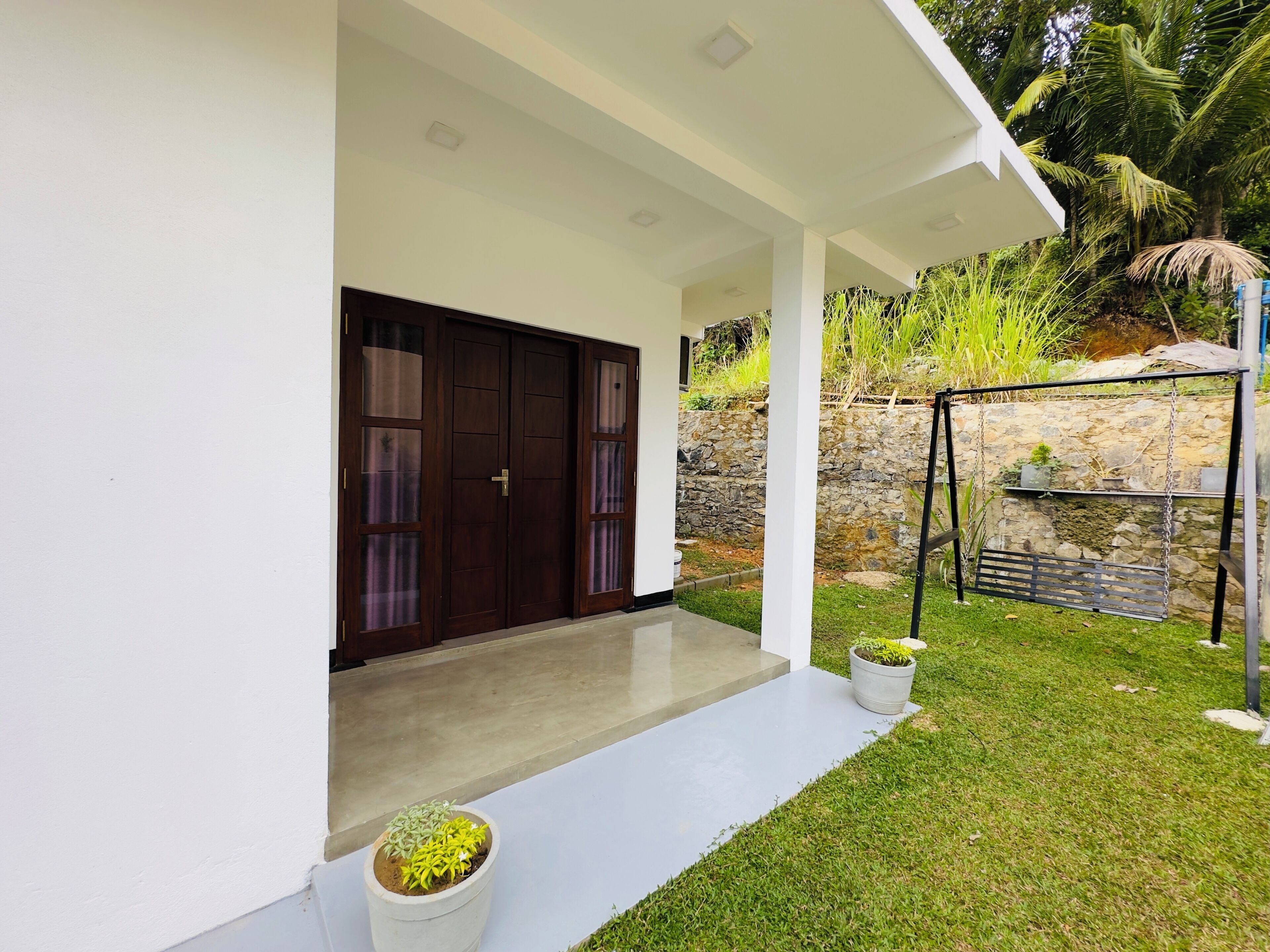 A modern house with a covered porch, a stone wall, and a swing set.