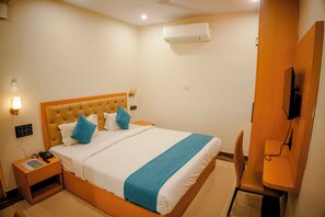 A hotel room with a bed, bedside table, lamp, and a TV mounted on the wall.