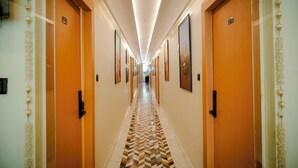A hotel hallway with wooden doors, numbered room signs, and framed artwork on the walls.