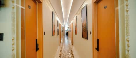 A hotel hallway with wooden doors, numbered room signs, and framed artwork on the walls.