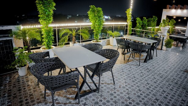 An outdoor seating area with tables and chairs, surrounded by potted plants and decorative lights.