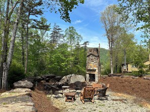 Una chimenea de piedra rodeada de mobiliario exterior en un área boscosa.