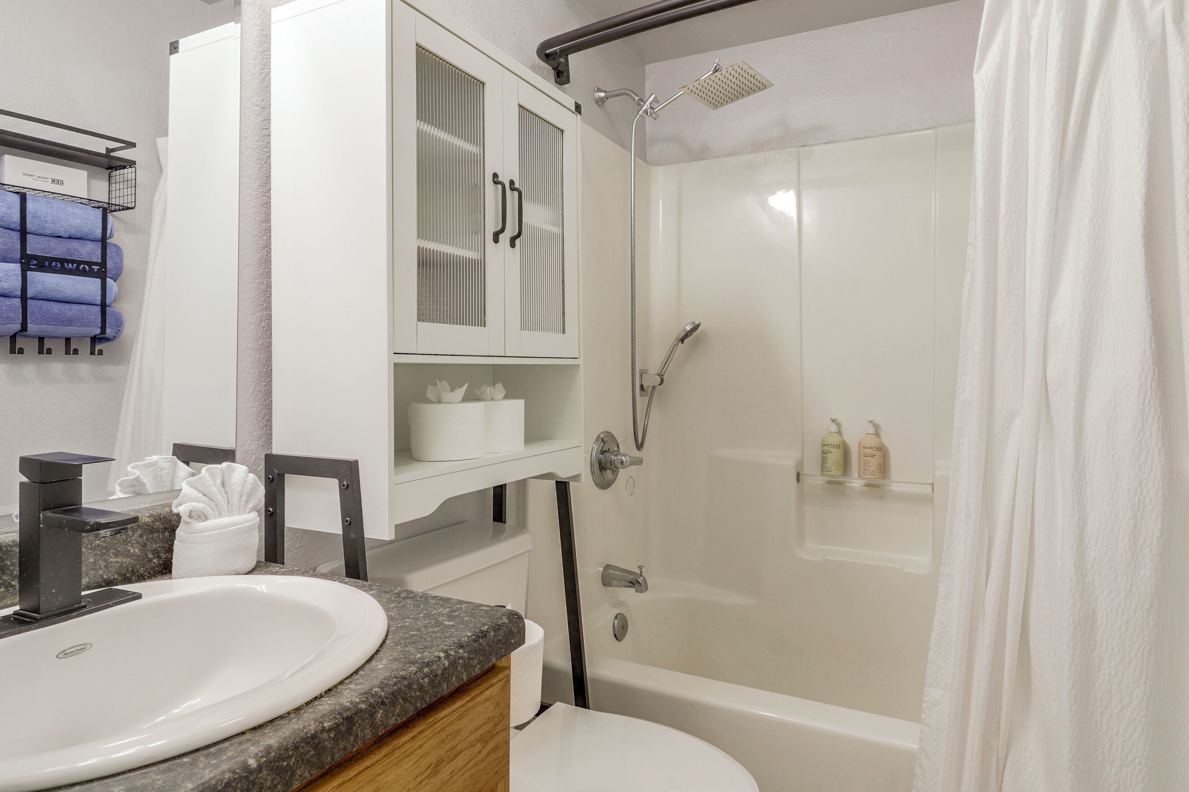 A bathroom with a white sink, a bathtub, and a shower. There are towels and toiletries on the shelves.