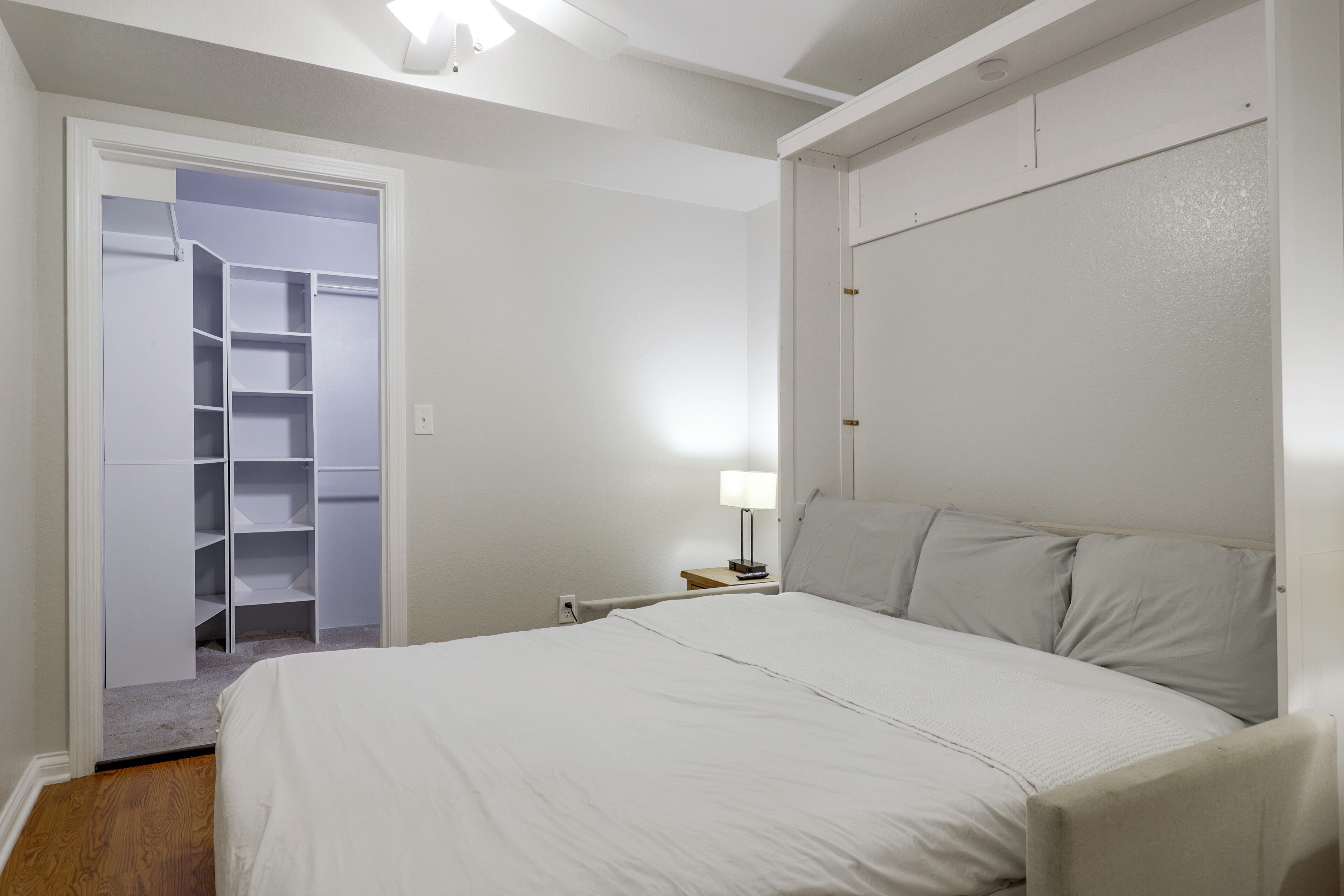 Et soveværelse med seng, natbord, lampe og et walk-in closet.