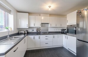 A modern kitchen with white cabinets, stainless steel appliances, and a black countertop. - Family-Friendly Townhouse Near Beach+2x carpark (Barry)