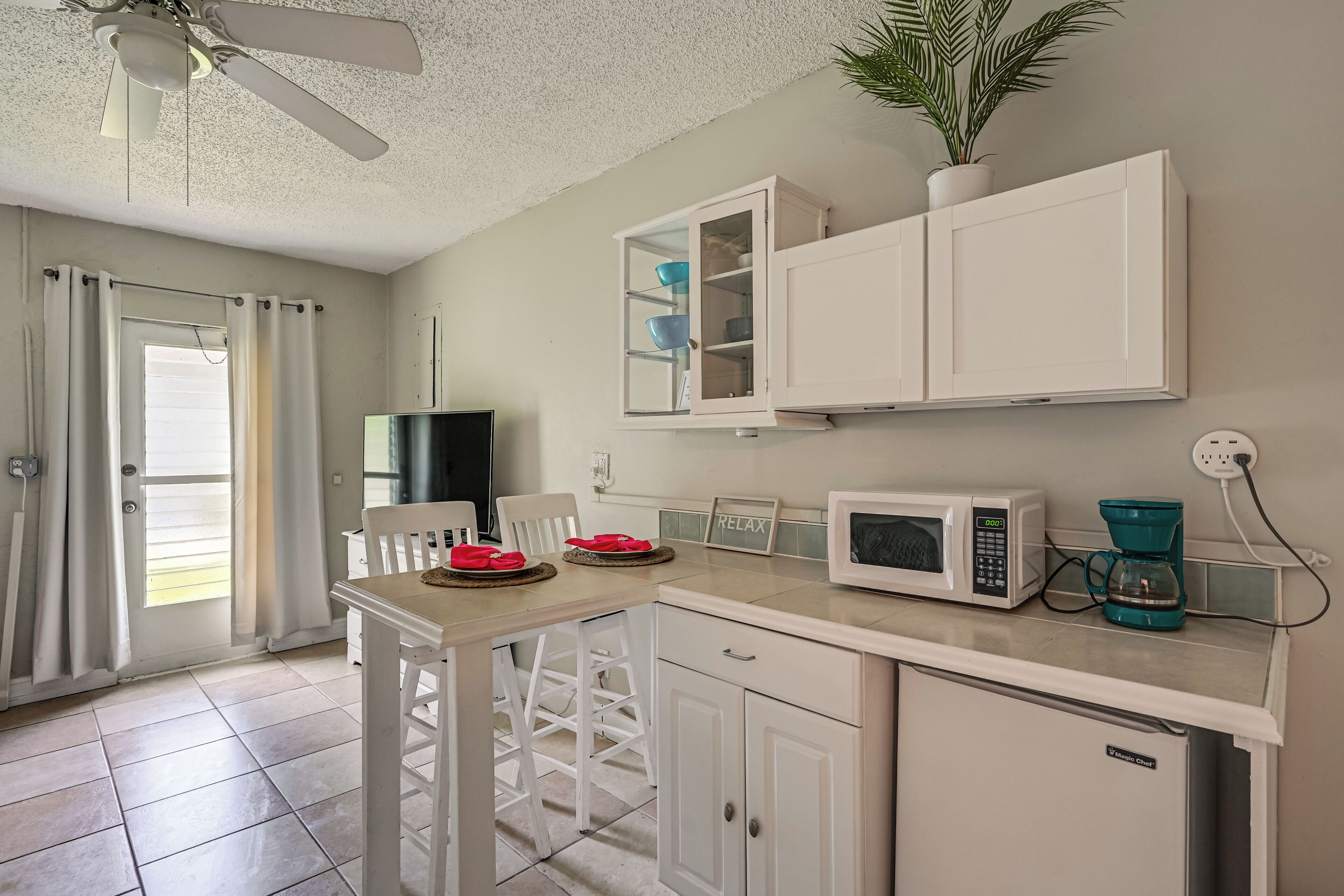 A compact kitchen with white cabinets, a microwave, a coffee maker, and a dining table with chairs.
