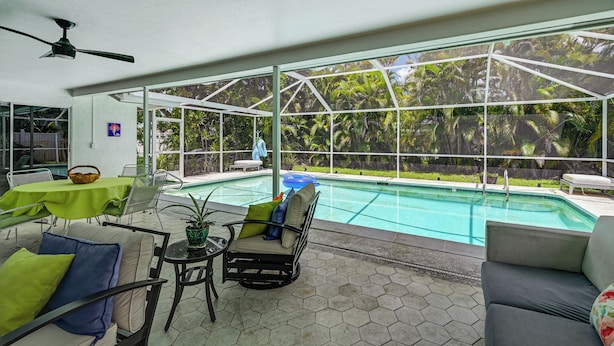 A covered outdoor area with a pool, seating, and a view of a tropical garden. - Lanai, Pool Access! Naples Studio Near Beach (Naples)