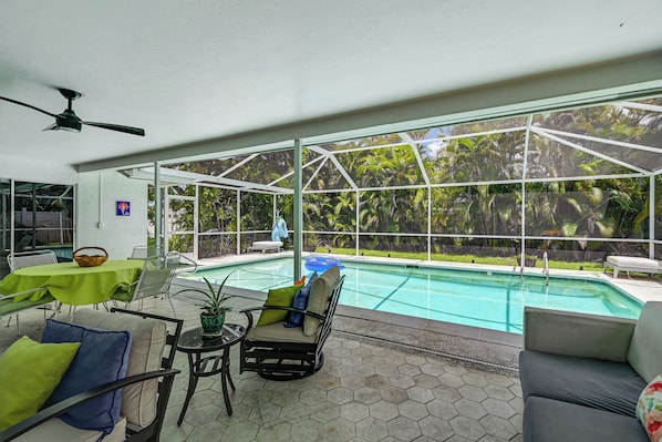 A covered outdoor area with a pool, seating, and a view of a tropical garden. - Lanai, Pool Access! Naples Studio Near Beach (Naples)