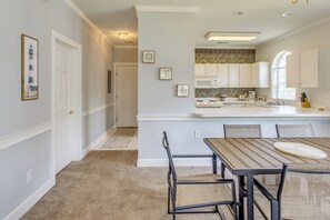 Una cocina moderna con armarios blancos, una isla central y una zona de comedor con mesa y sillas de madera.