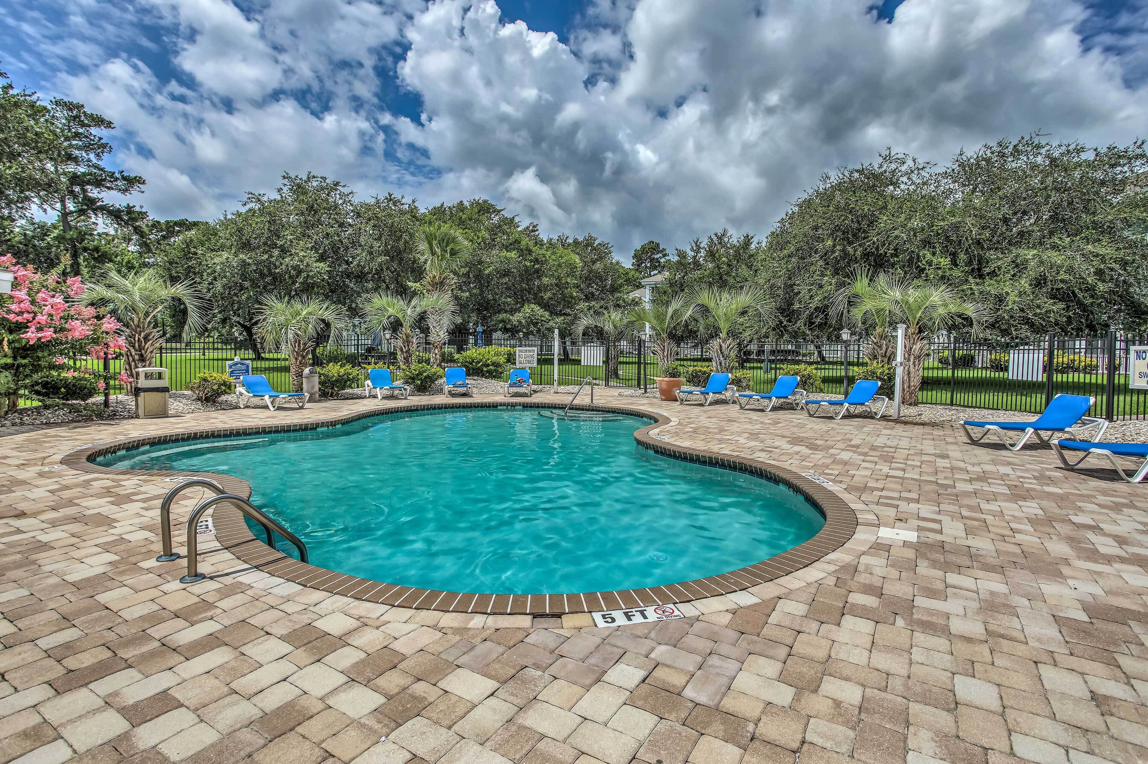 A swimming pool with blue water, surrounded by a brick patio and blue lounge chairs.