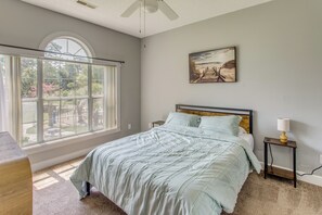 A bedroom with a large window, a bed with a headboard, a bedside table with a lamp, and a painting on the wall. - 6 Pools, Golf Course! Myrtle Beach Family Condo (Myrtle Beach)