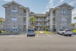 A multi-story building with a stone facade, parking lot, and two SUVs parked in front. - 6 Pools, Golf Course! Myrtle Beach Family Condo (Myrtle Beach)