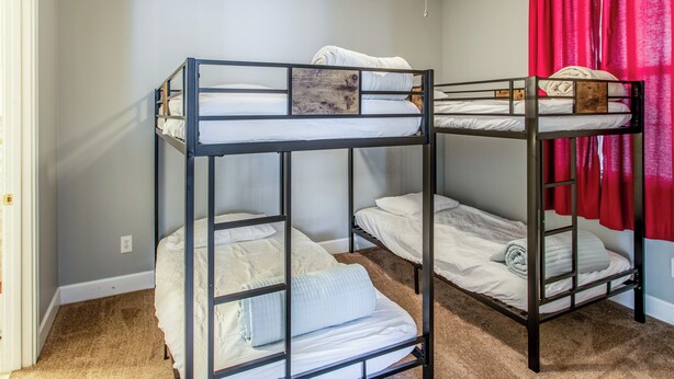 Een slaapkamer met stapelbed, plafondventilator, vloerbedekking en een rood gordijn.