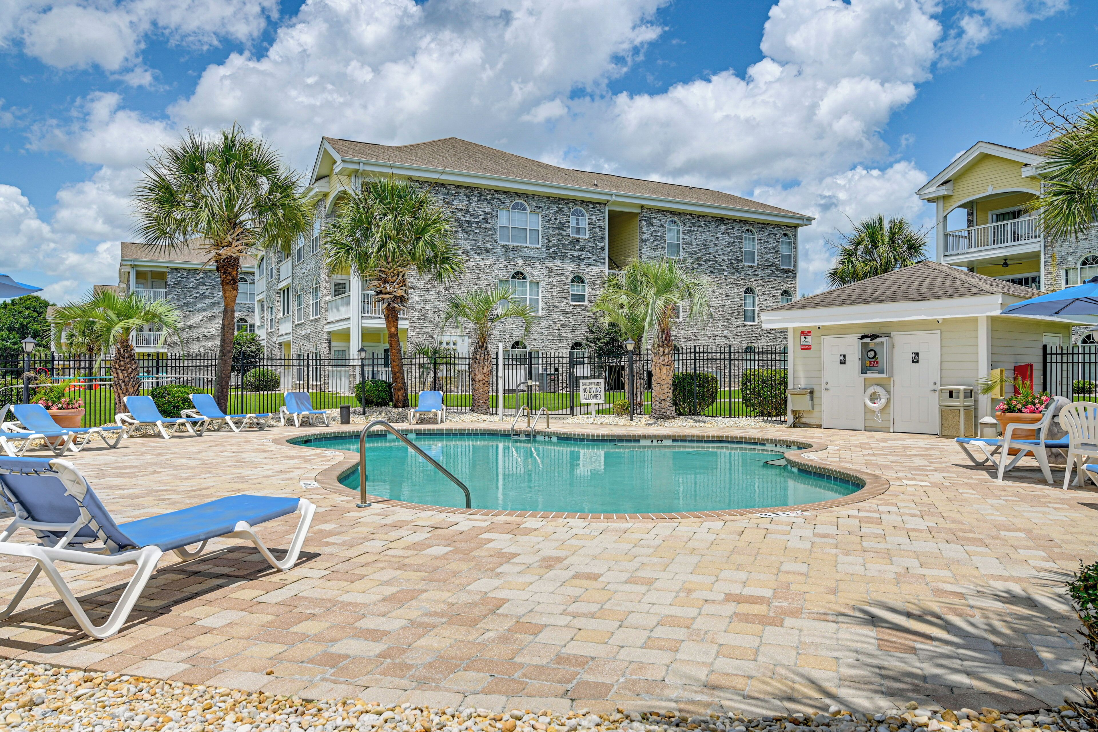 A pool area with lounge chairs, a pool, and a building with stone facade and balconies.