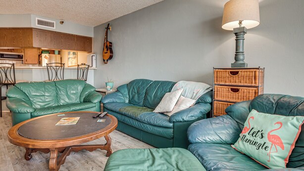 A living room with green leather sofas, a wooden coffee table, a lamp, and a guitar on the wall. - Beachfront Condo! Heated Pool, Ocean-view Balcony (Daytona Beach Shores)