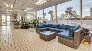 A spacious indoor area with a large sectional sofa, a coffee table, and a variety of potted plants. - Beachfront Condo! Heated Pool, Ocean-view Balcony (Daytona Beach Shores)