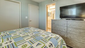 A bedroom with a bed, a dresser, a television, and a door leading to a bathroom. - Beachfront Condo! Heated Pool, Ocean-view Balcony (Daytona Beach Shores)