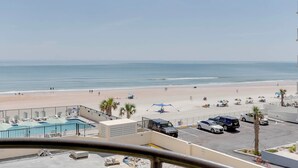 A beach view from a balcony with a pool, umbrellas, and parked cars. - Beachfront Condo! Heated Pool, Ocean-view Balcony (Daytona Beach Shores)