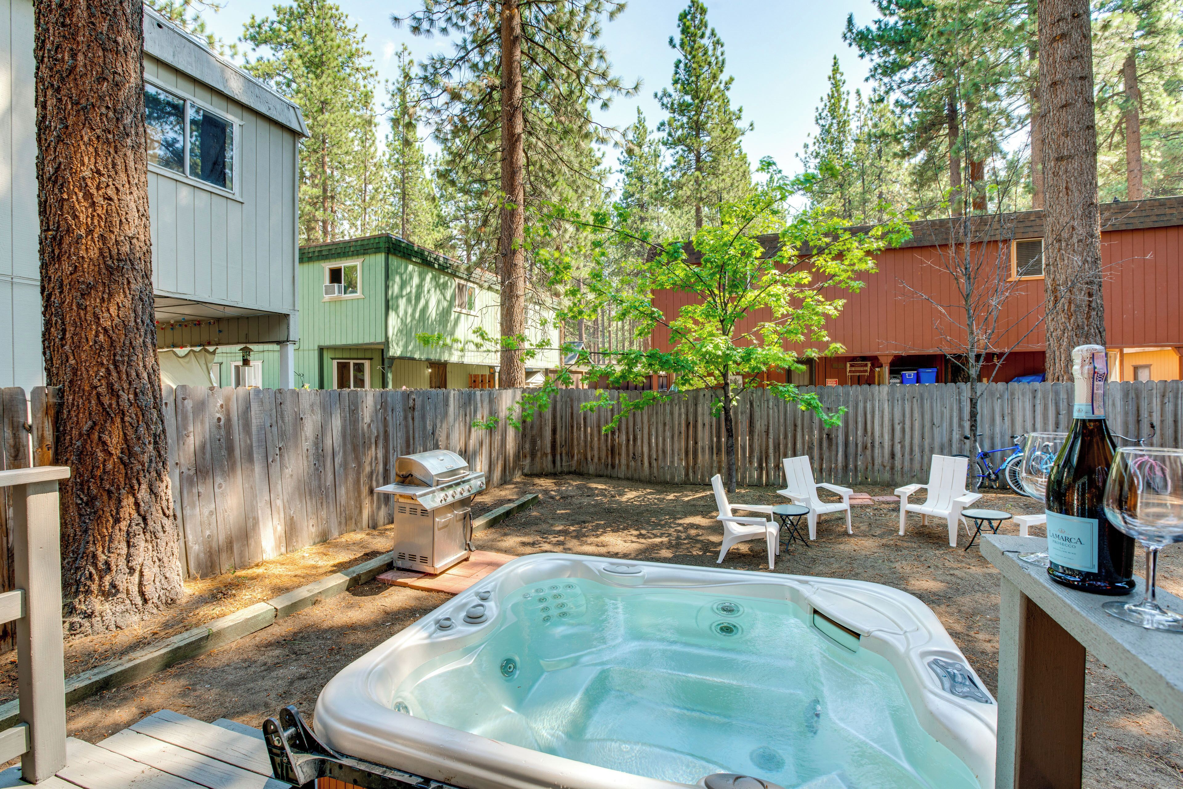 Un patio trasero con jacuzzi, mobiliario exterior, una parrilla y una valla de madera.