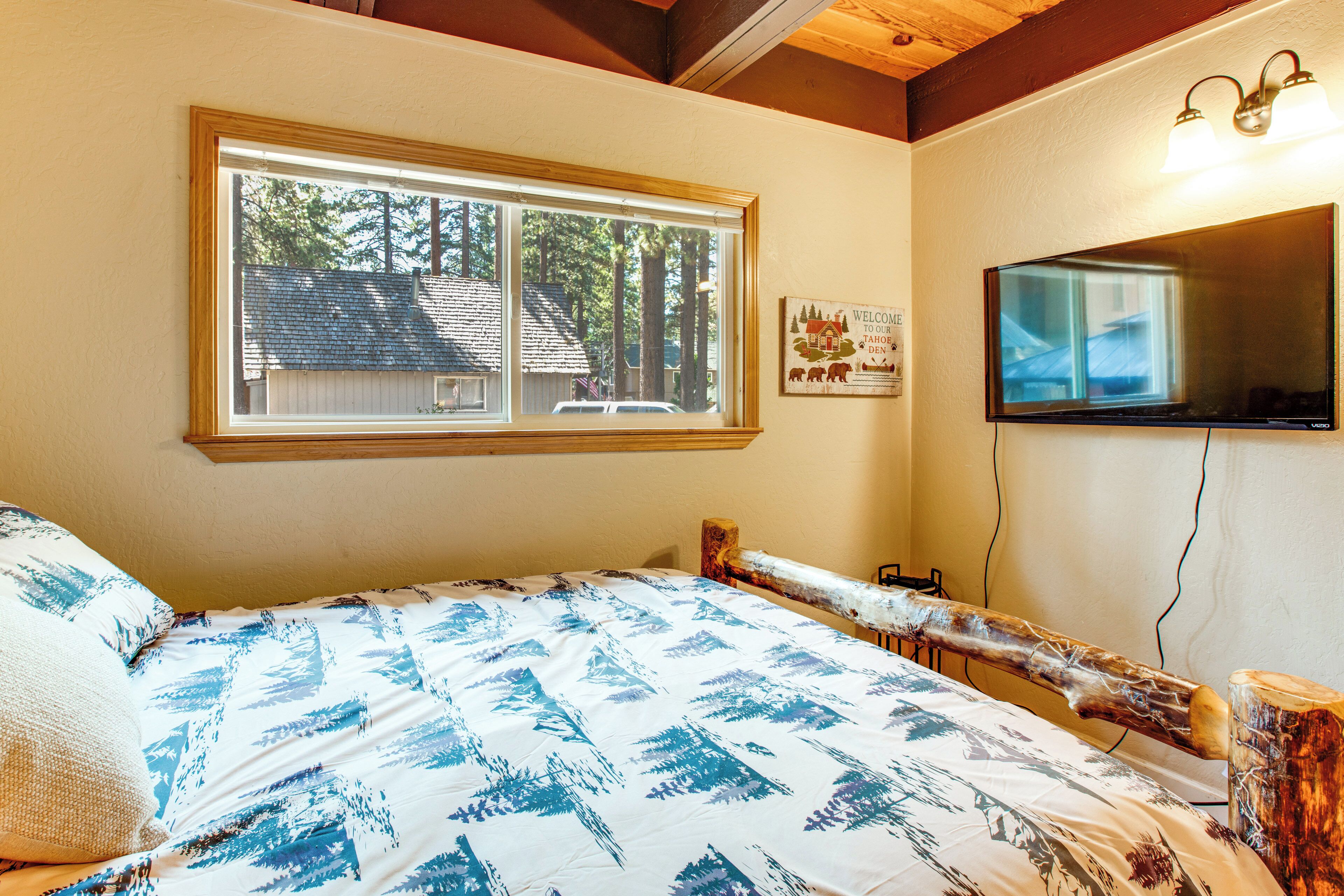 A bedroom with a large bed, a window with a view of trees, a mounted TV, and a welcome sign.