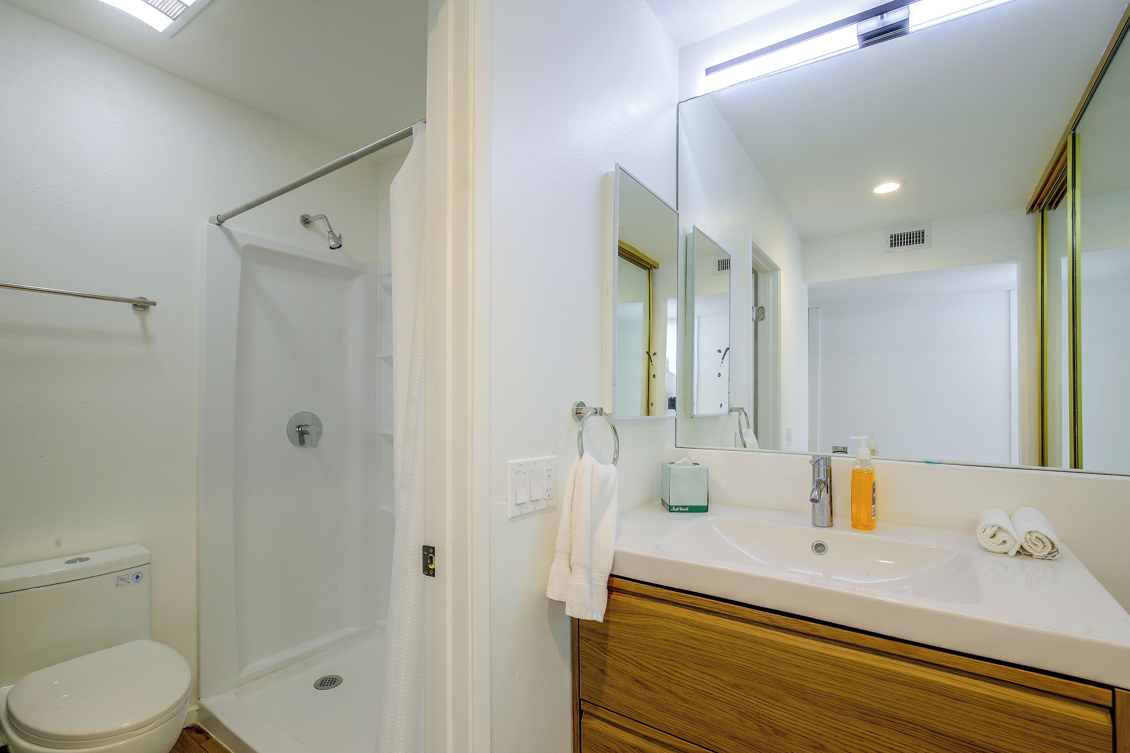 A bathroom with a shower, toilet, sink, and mirror.