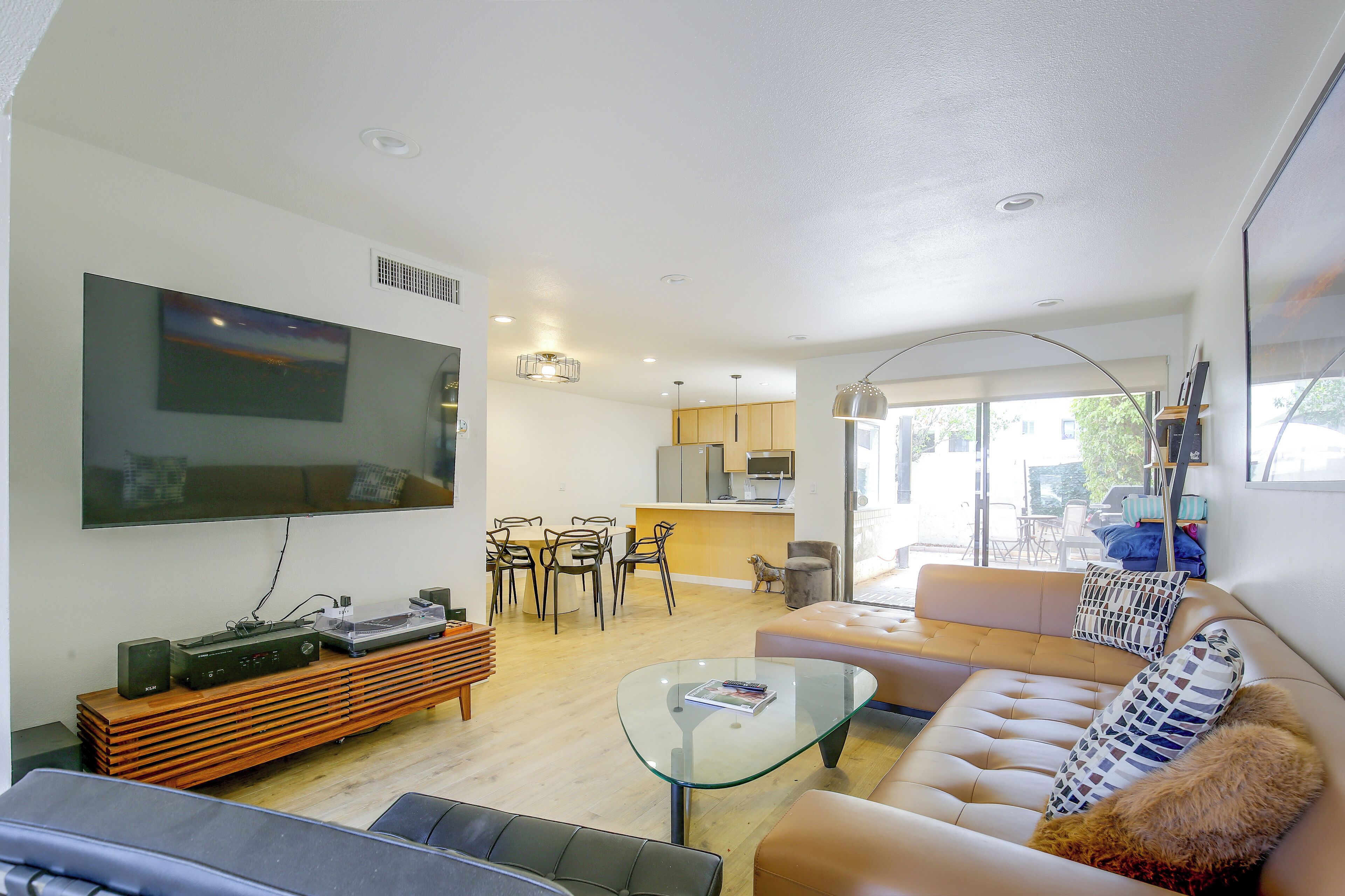 A modern living room with a flat-screen TV, a glass coffee table, a sofa, and a dining area with chairs.