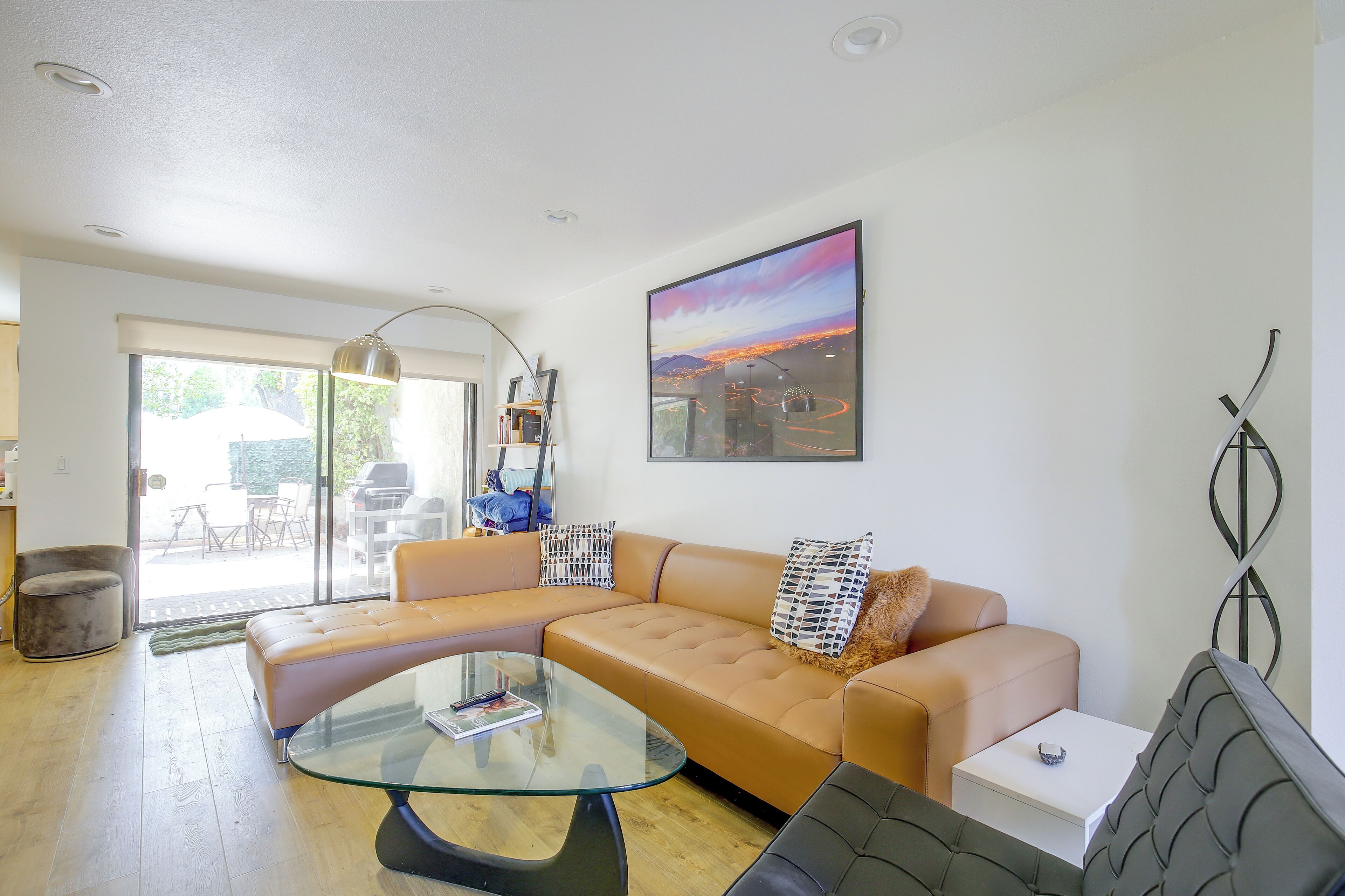 A modern living room with a glass coffee table, a tan sofa, and a large window.