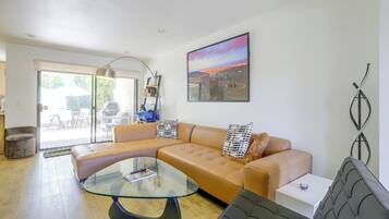 A modern living room with a glass coffee table, a tan sofa, and a large window.