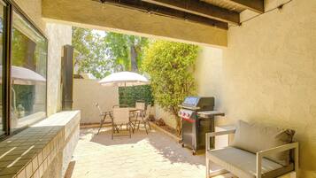 An outdoor patio with a grill, a table with chairs, and a cushioned bench.