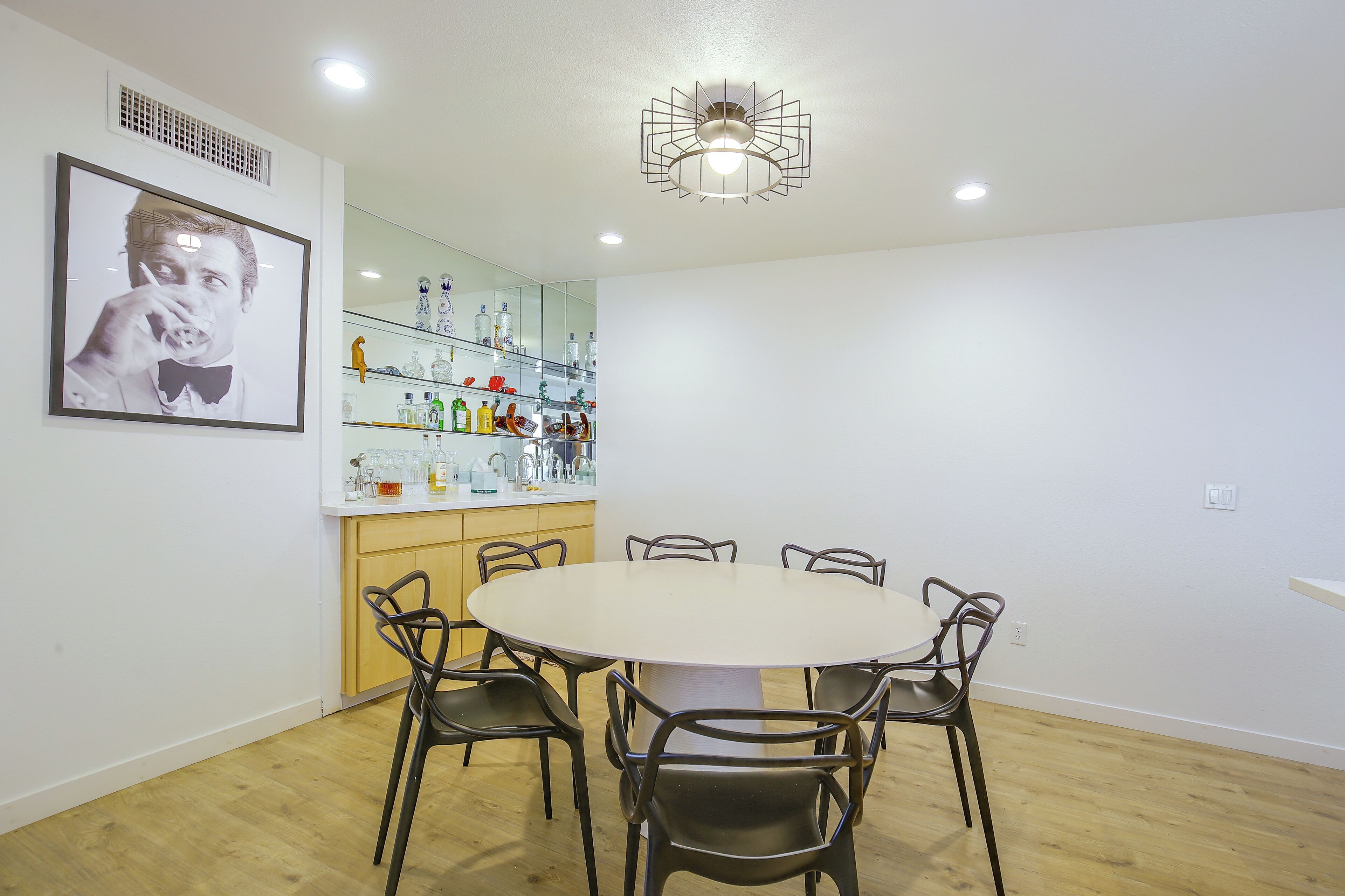 A dining area with a round table and four chairs, a kitchen area with a mirrored backsplash, and a ceiling light fixture.