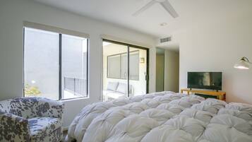 A bedroom with a large bed, a chair, a television, and a ceiling fan.