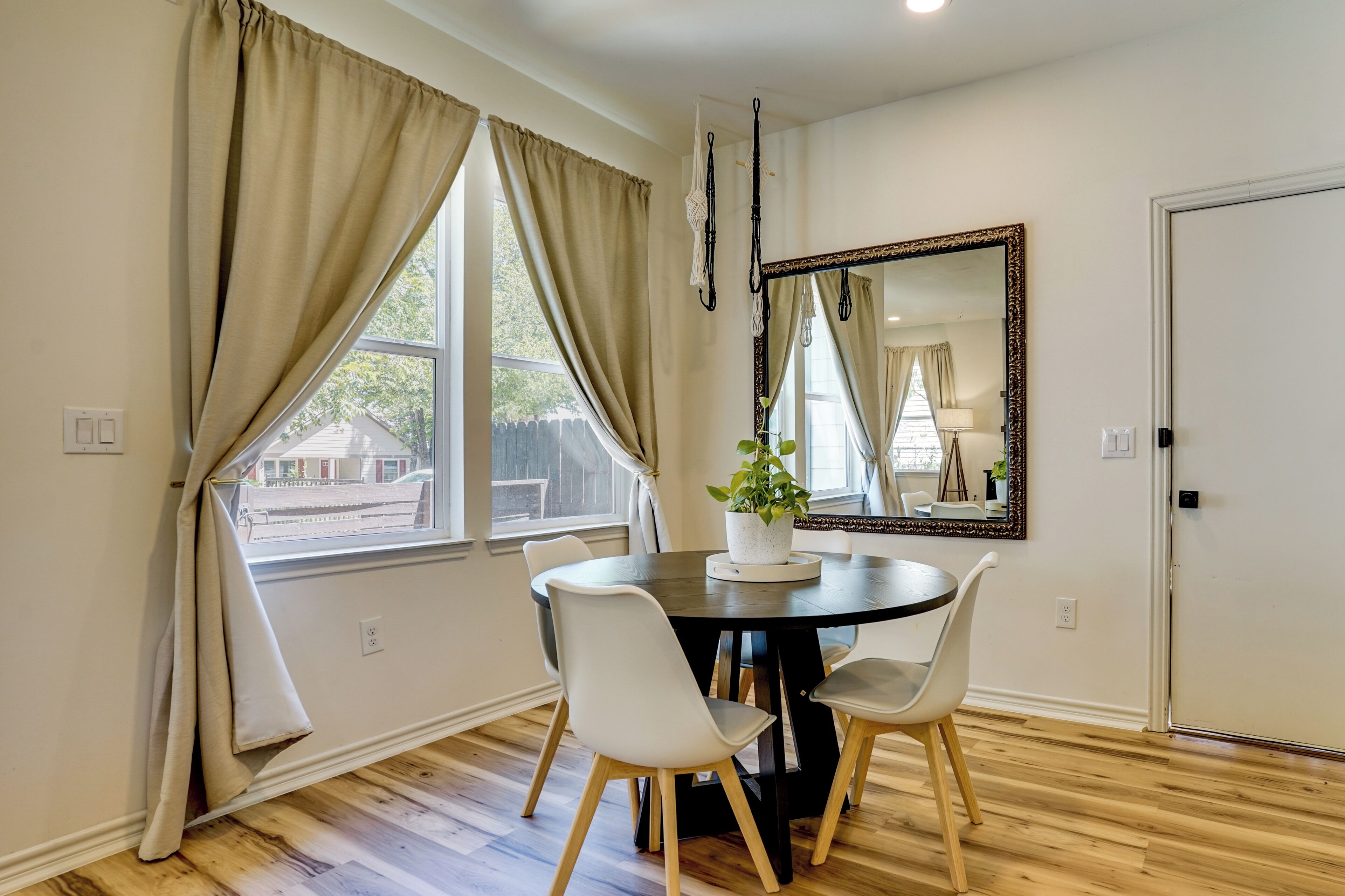 A dining area with a round table, two chairs, a potted plant, and a large mirror on the wall.