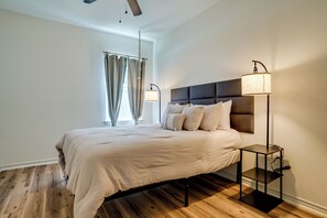 A bedroom with a bed, a bedside table, a floor lamp, and a window with curtains.