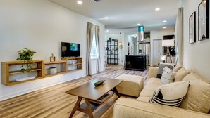 A modern living room with a wooden floor, a sofa set, a coffee table, a TV, and a bookshelf. - Historic Southside Fort Worth Home w/ Fenced Yard! (Fort Worth)