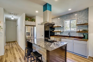 A modern kitchen with a central island, stainless steel appliances, and a window overlooking the outdoors.