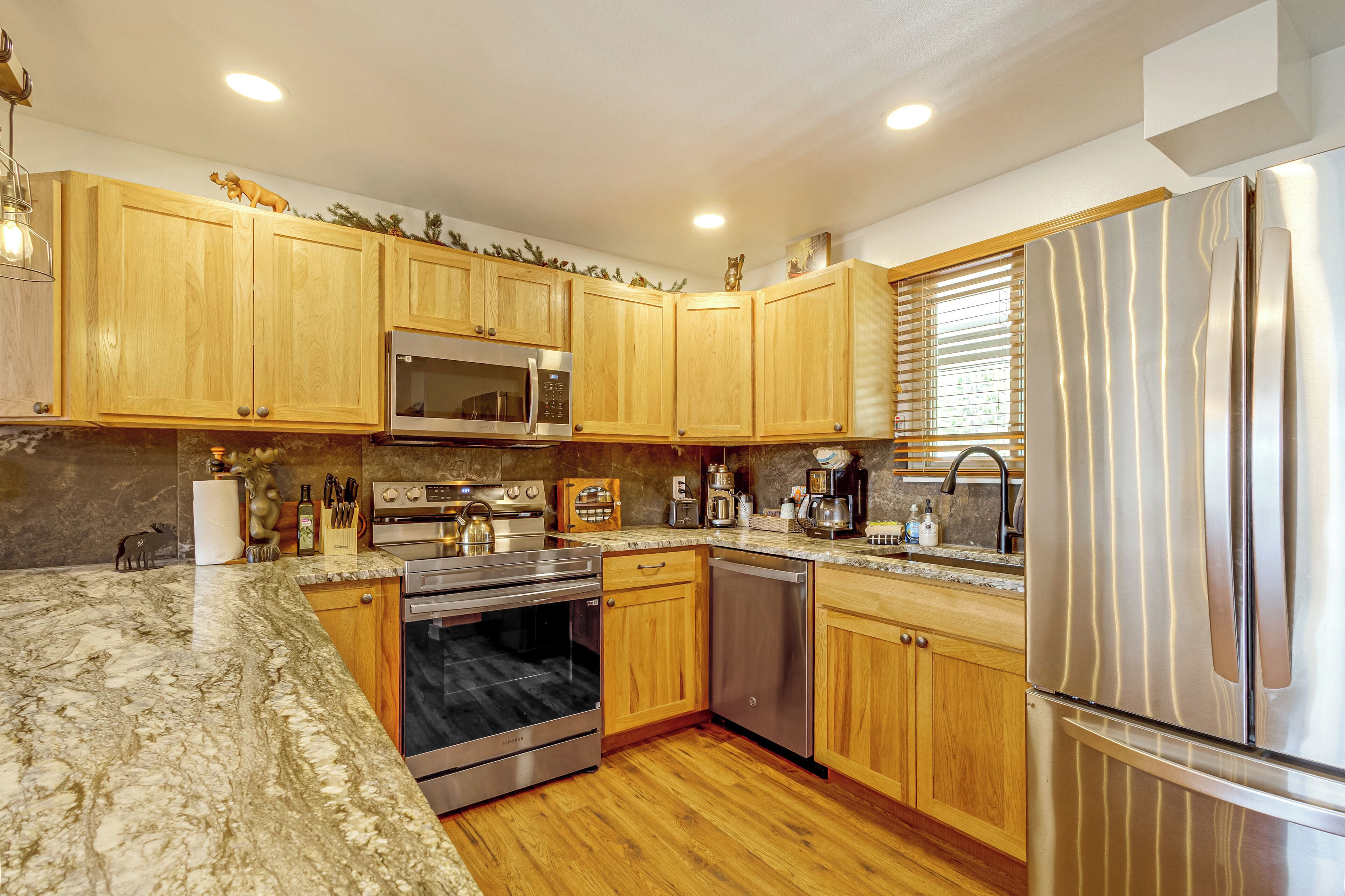 A modern kitchen with wooden cabinets, stainless steel appliances, and a marble countertop.